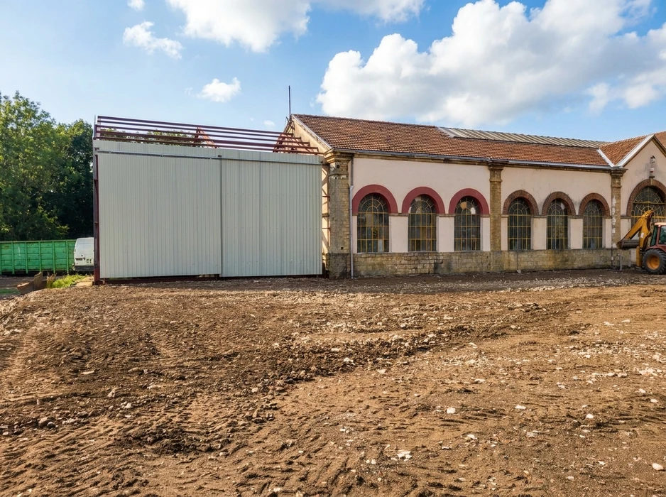 Chantier de réhabilitation d'un bâtiment industriel ancien à façade crépi beige, fenêtres en arc en plein cintre avec encadrements en brique rouge
