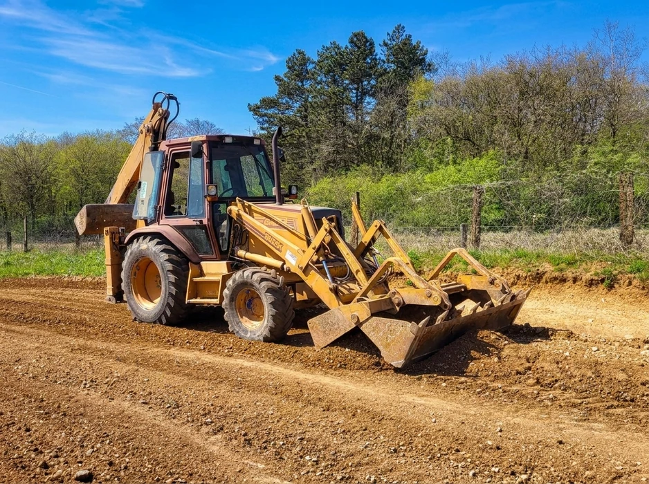 Chantier de construction extérieur avec compacteur à cylindre vibrant jaune en premier plan compactant sol terreux