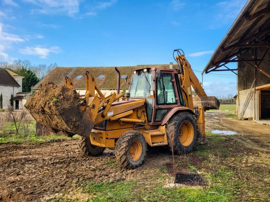 Pelleteuse de chantier jaune en action, chargeuse-pelleteuse (backhoe loader) de marque JCB, modèle 3CX, opérant en milieu rural