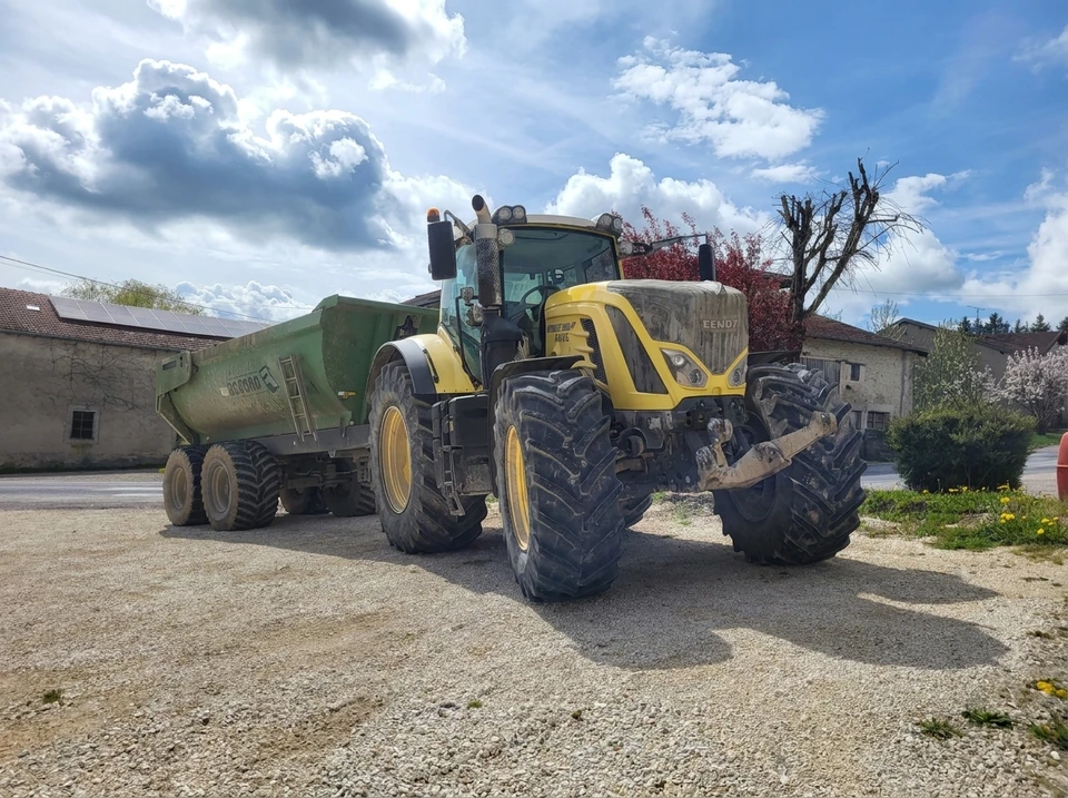 Chantier extérieur en zone boisée avec camion-benne déchargeant du gravier gris sur terrain herbeux